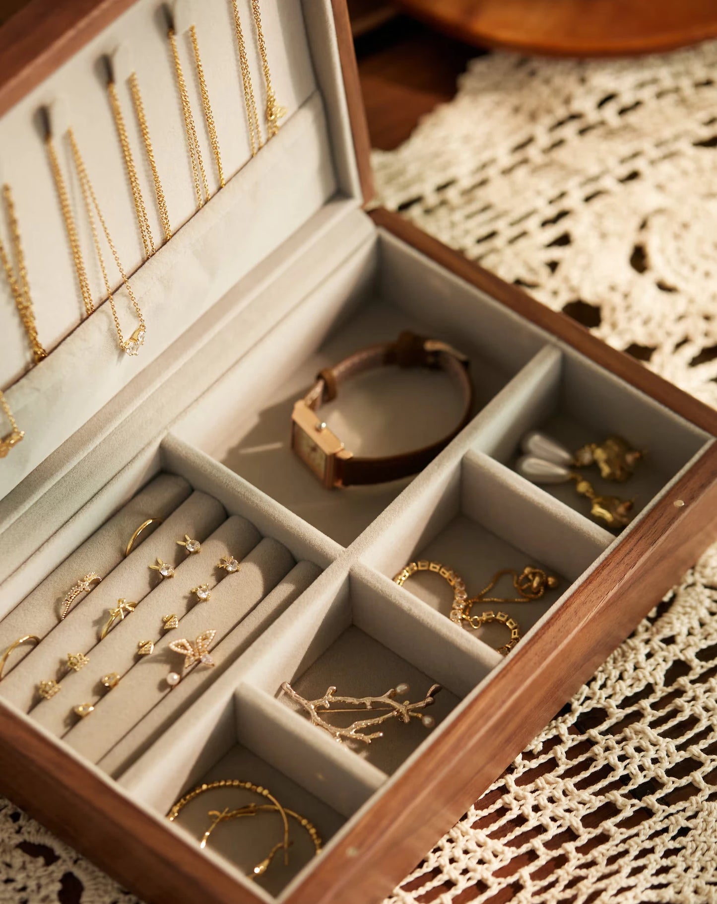 Open walnut jewelry box filled with gold jewelry on a lace mat.