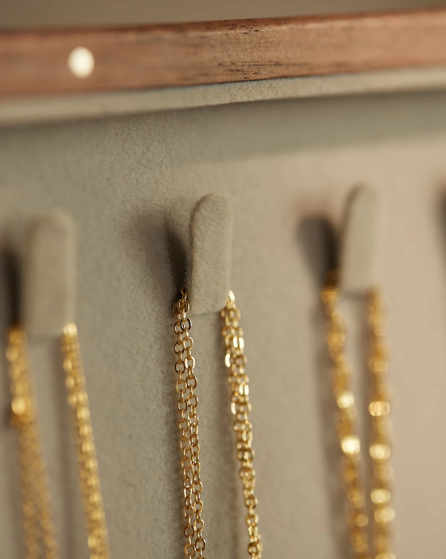 Close-up of gold necklaces hanging on soft hooks inside a jewelry box.