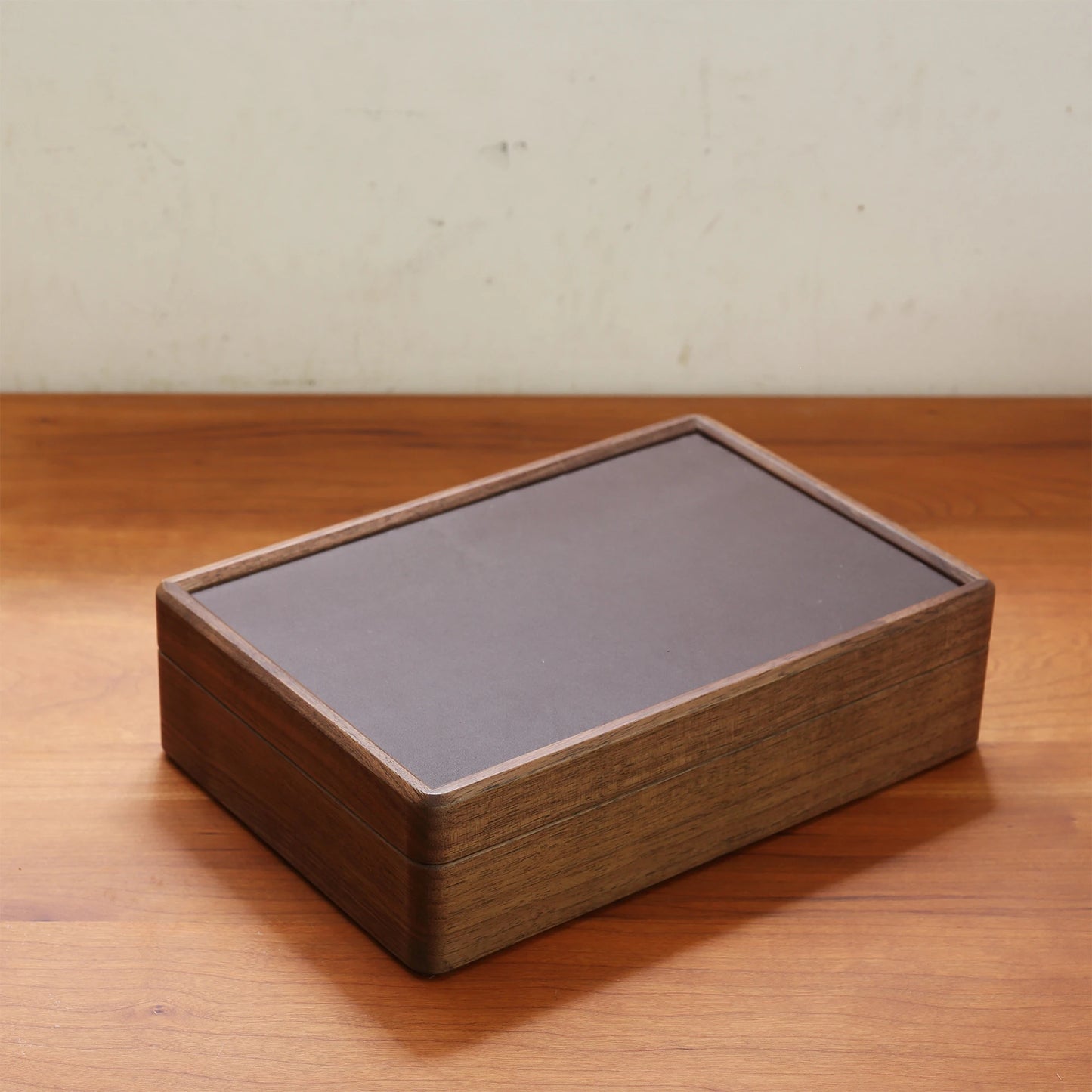 A closed dark walnut wood jewelry box with leatherette top on a desk.