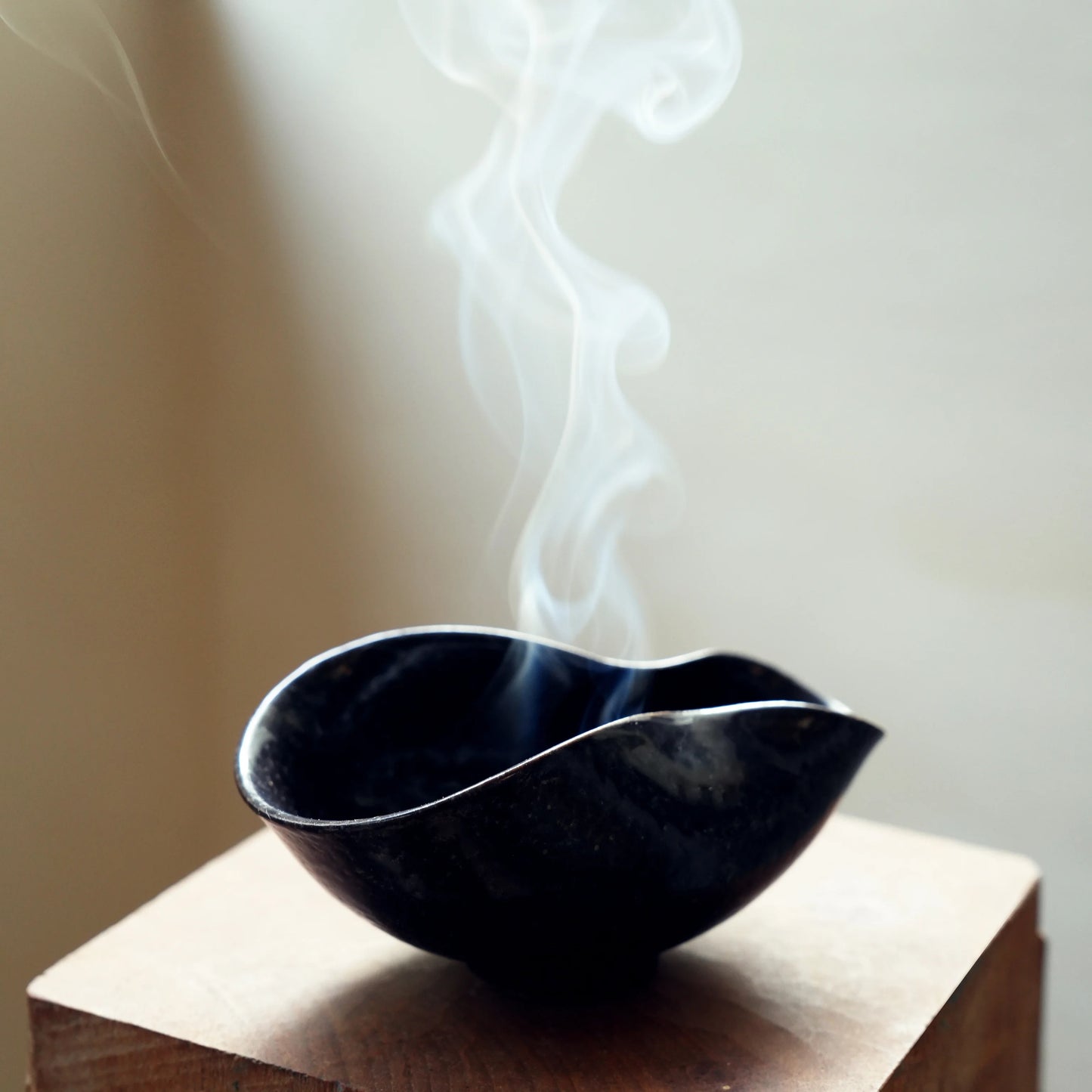 Close-up of smoke curling from an organic wabi-sabi incense bowl.