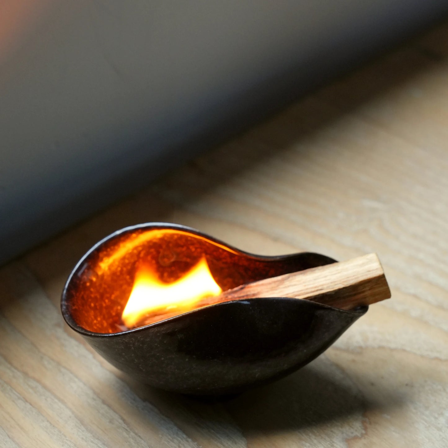 A Palo Santo stick burning brightly inside a dark ceramic ritual bowl.