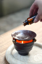 Hand dropping essential oil into ceramic aromatherapy burner