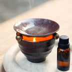 Lit ceramic oil burner with rising steam and essential oil bottle