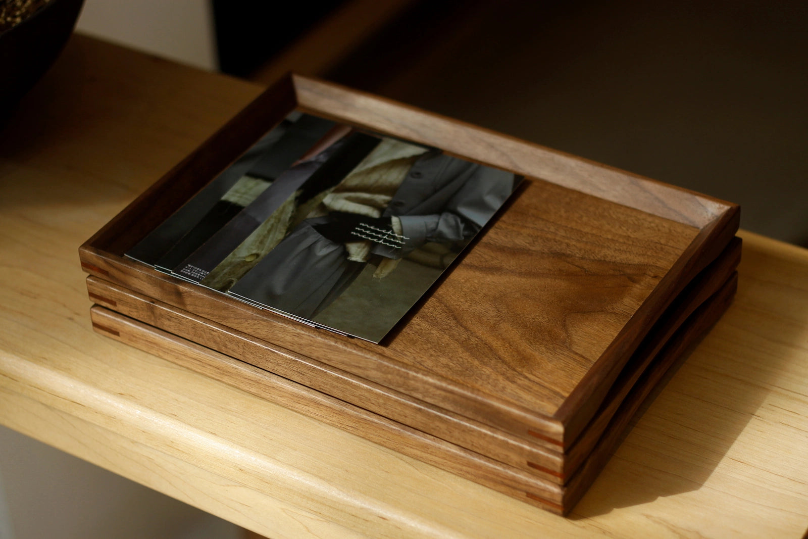 Walnut wood tray holding magazine on wood shelf, dark interior
