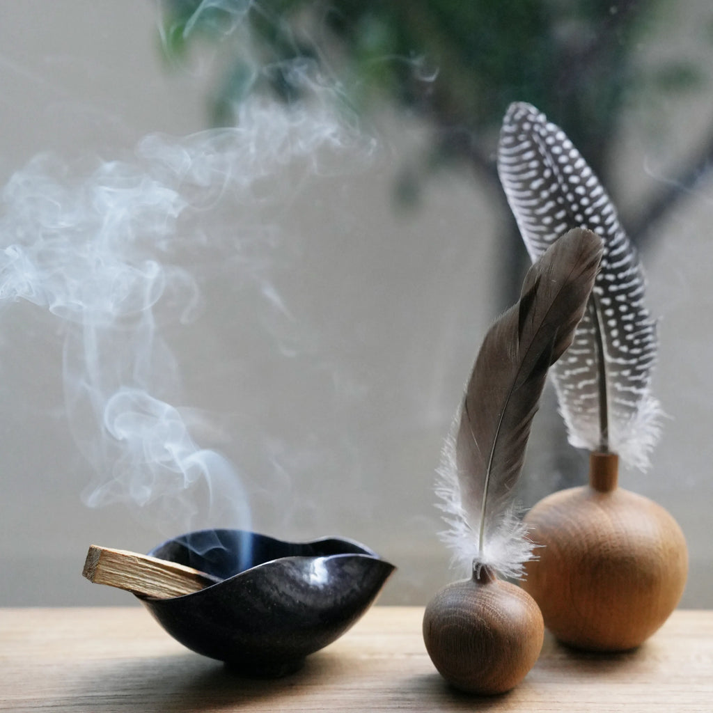 A smoldering Palo Santo stick in a ceramic bowl with decorative feathers.