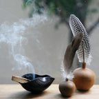 A smoldering Palo Santo stick in a ceramic bowl with decorative feathers.