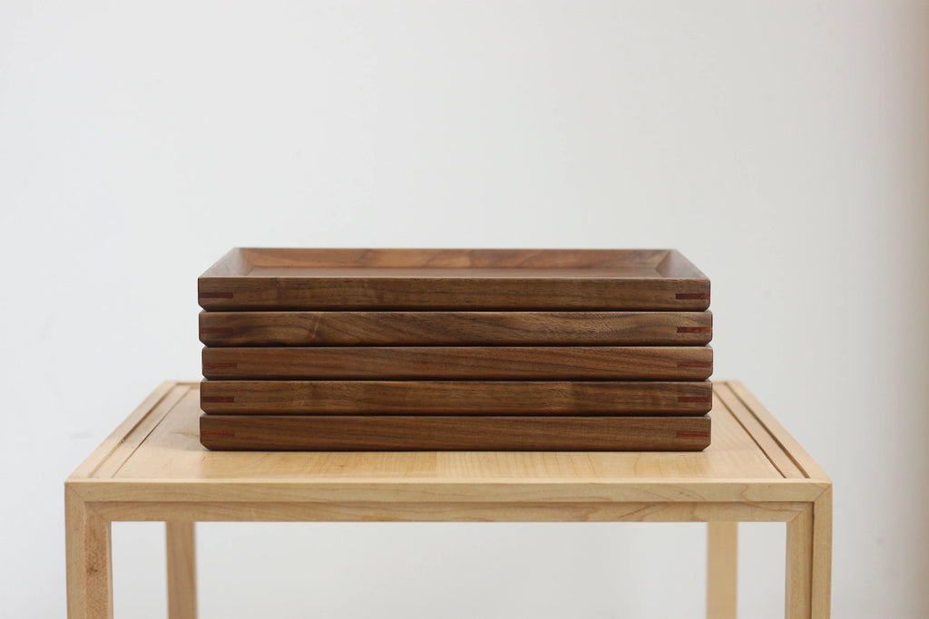 Five handcrafted walnut wood trays stacked on light wood stand