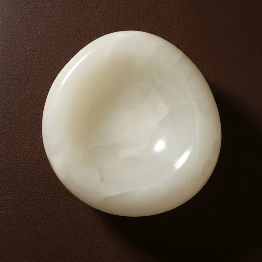 A top-down overhead shot of the polished alabaster bowl, emphasizing its milky, translucent quality against a textured dark brown surface.