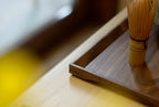 Corner detail of walnut tray with bamboo matcha whisk, warm light