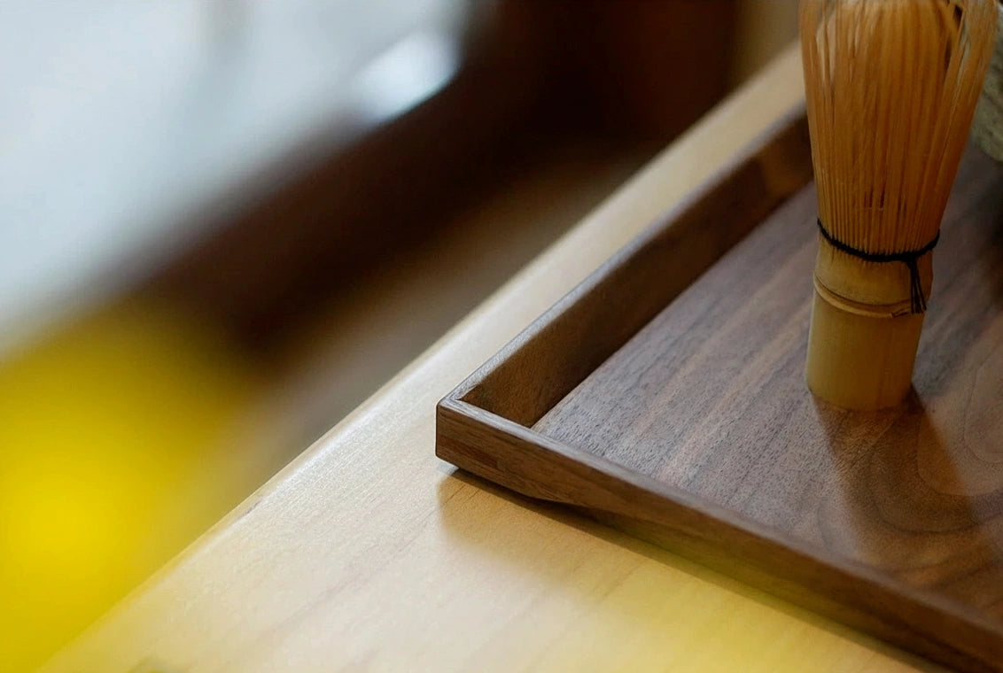 Corner detail of walnut tray with bamboo matcha whisk, warm light