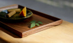 Walnut wood tray with green leaves and ceramic plate, sunlit table