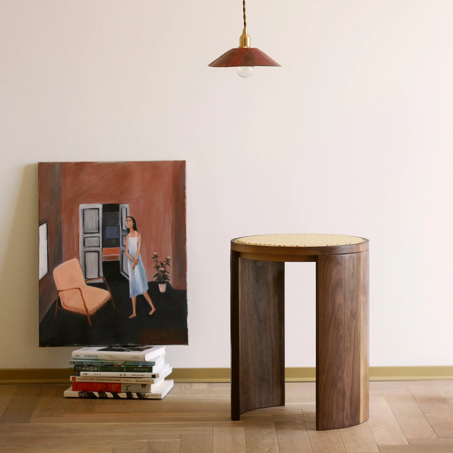 A walnut and rattan stool styled next to a painting in an artful home.