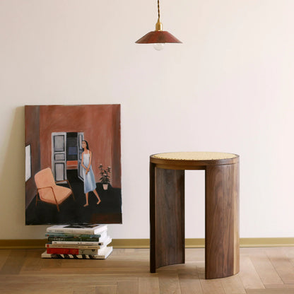 A walnut and rattan stool styled next to a painting in an artful home.