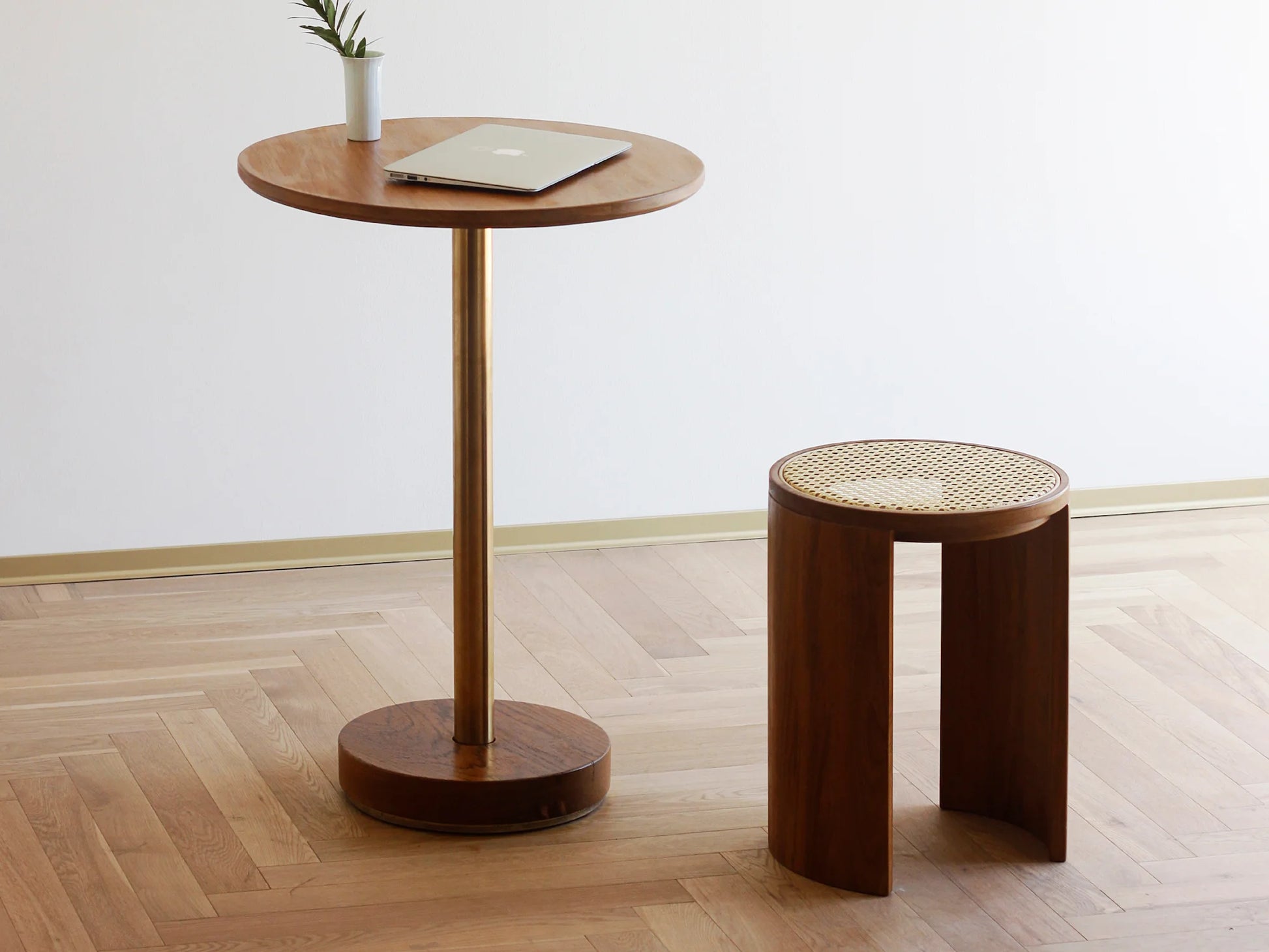 A wood and rattan stool used as a side table next to a minimalist bar table.