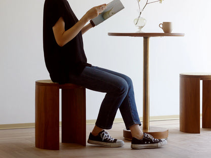 A person sitting on the handwoven rattan stool while reading a magazine.