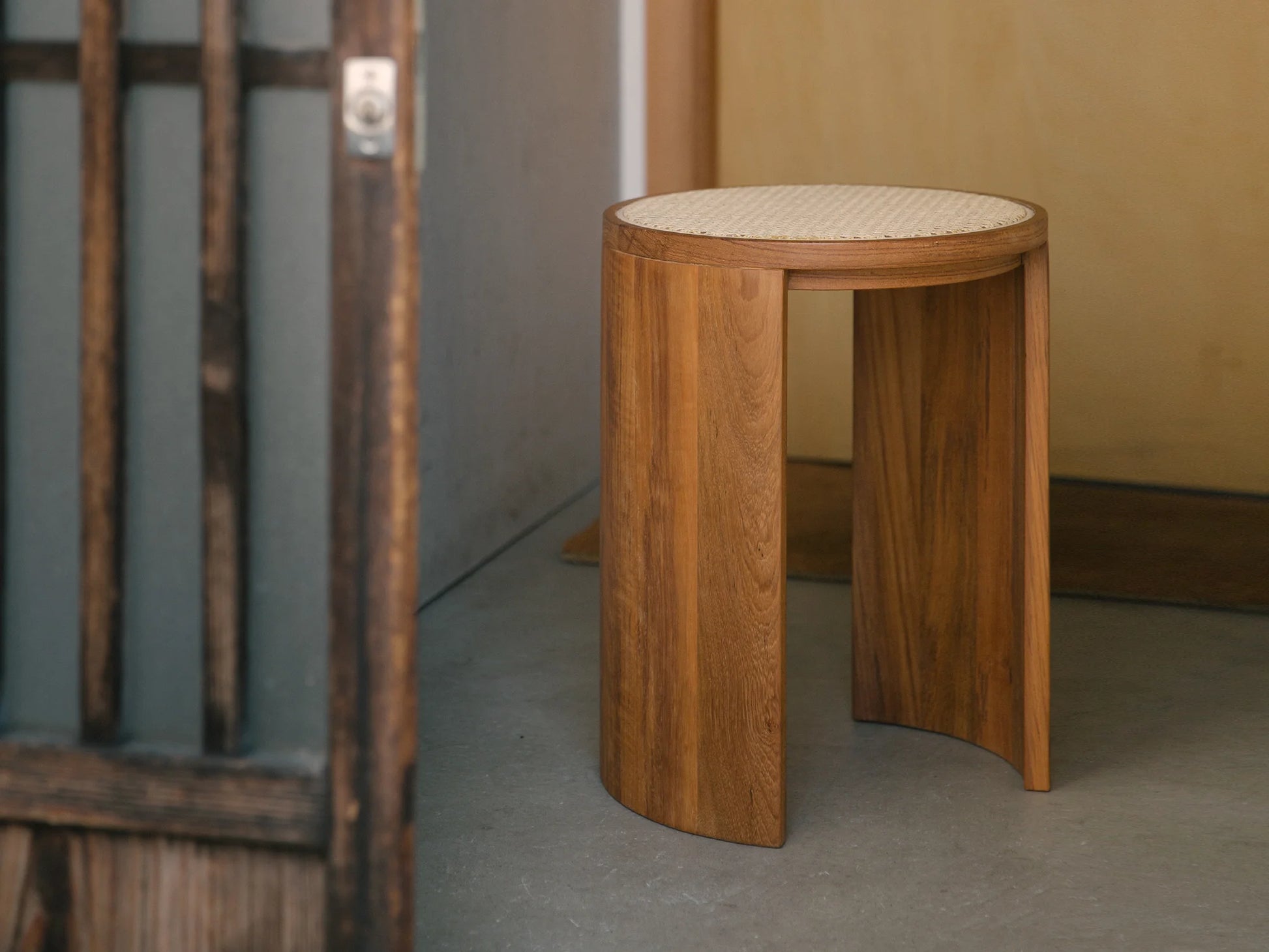 A solid wood stool with a woven rattan top in a modern entryway.