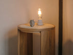A teak wood and rattan stool used as a bedside table with a small lamp.