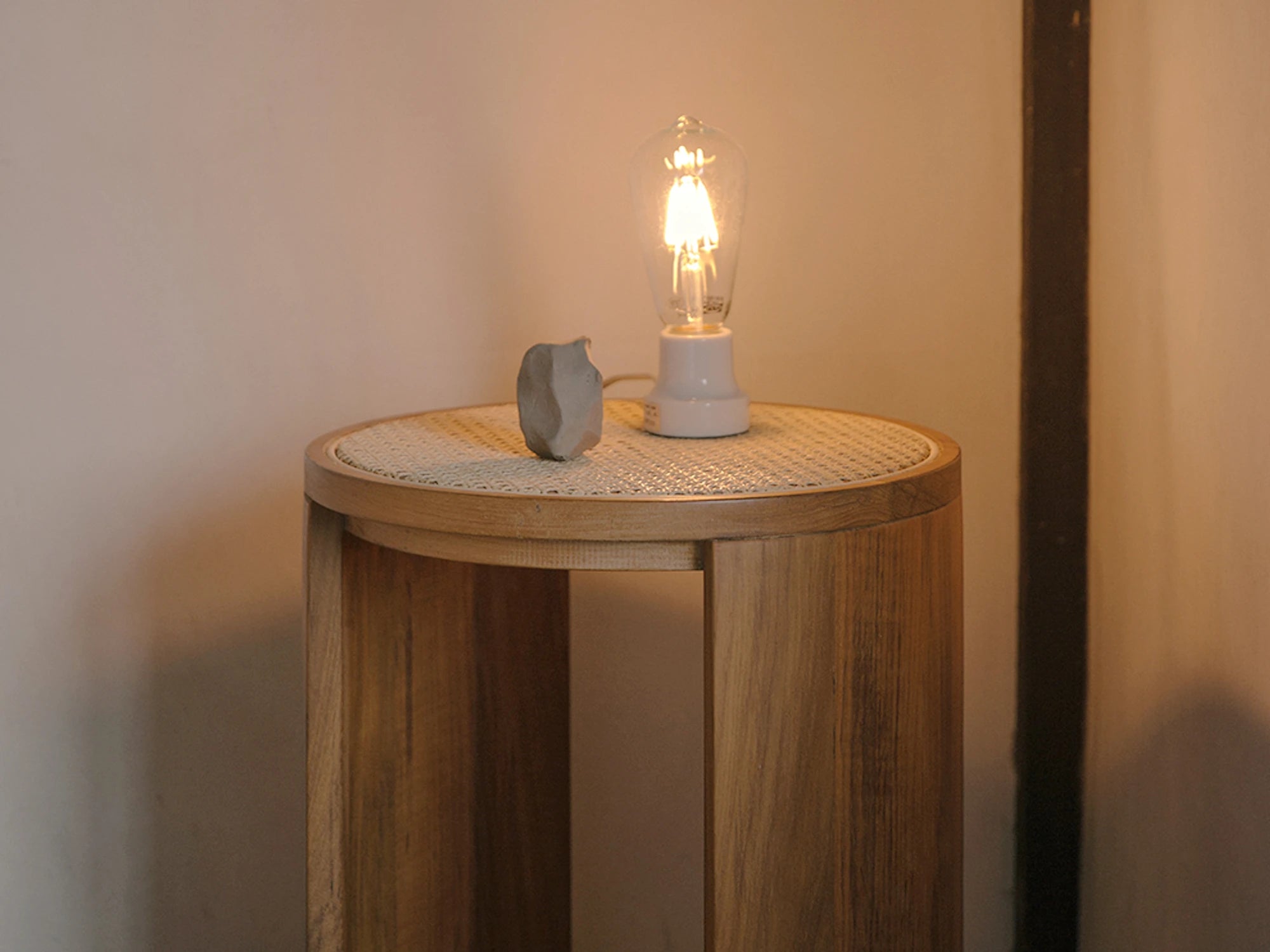 A teak wood and rattan stool used as a bedside table with a small lamp.