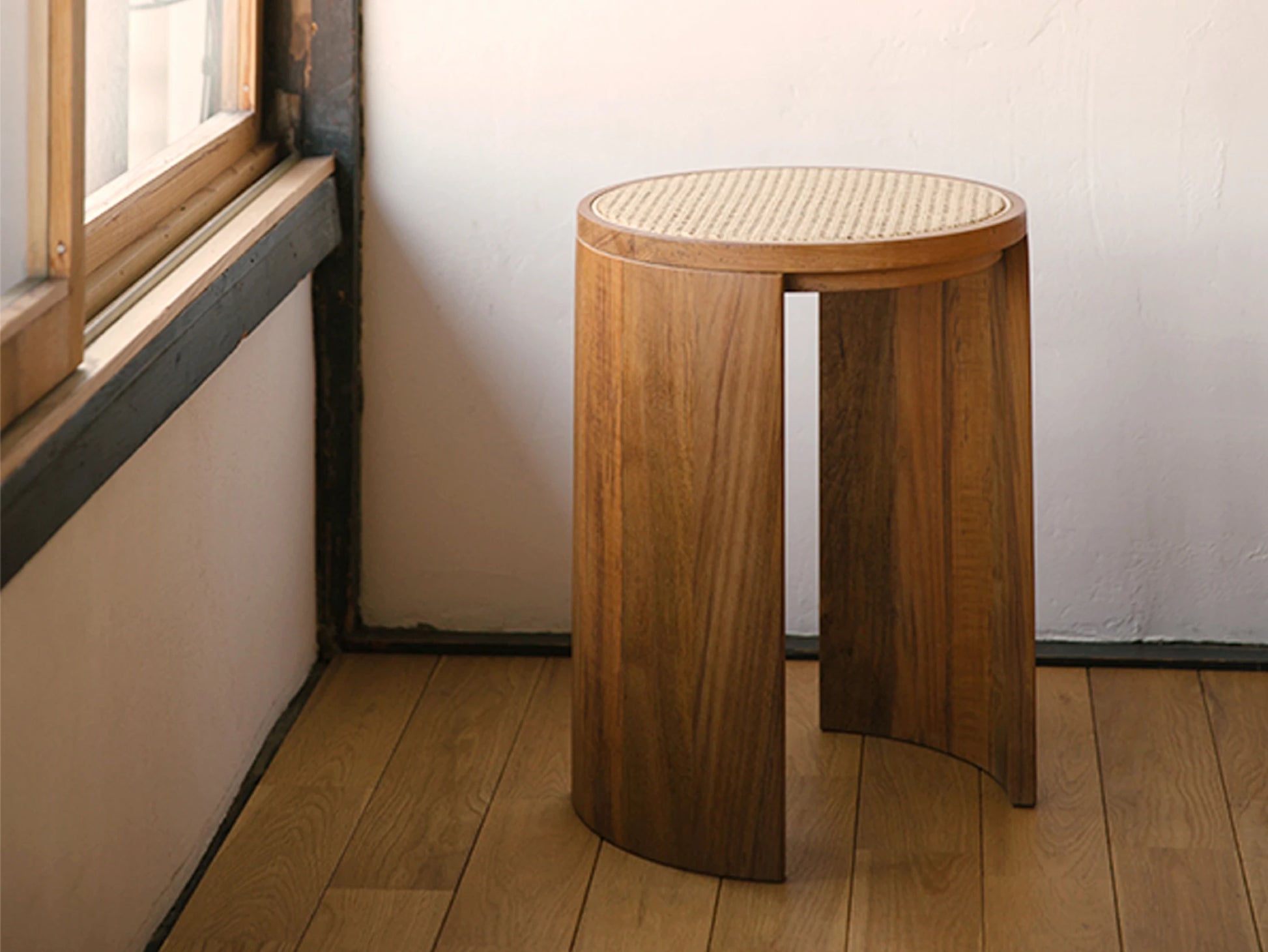 A minimalist rattan and wood stool styled in a corner by a window.