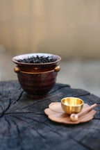 Ceramic oil burner with dried tea leaves on dark wood surface