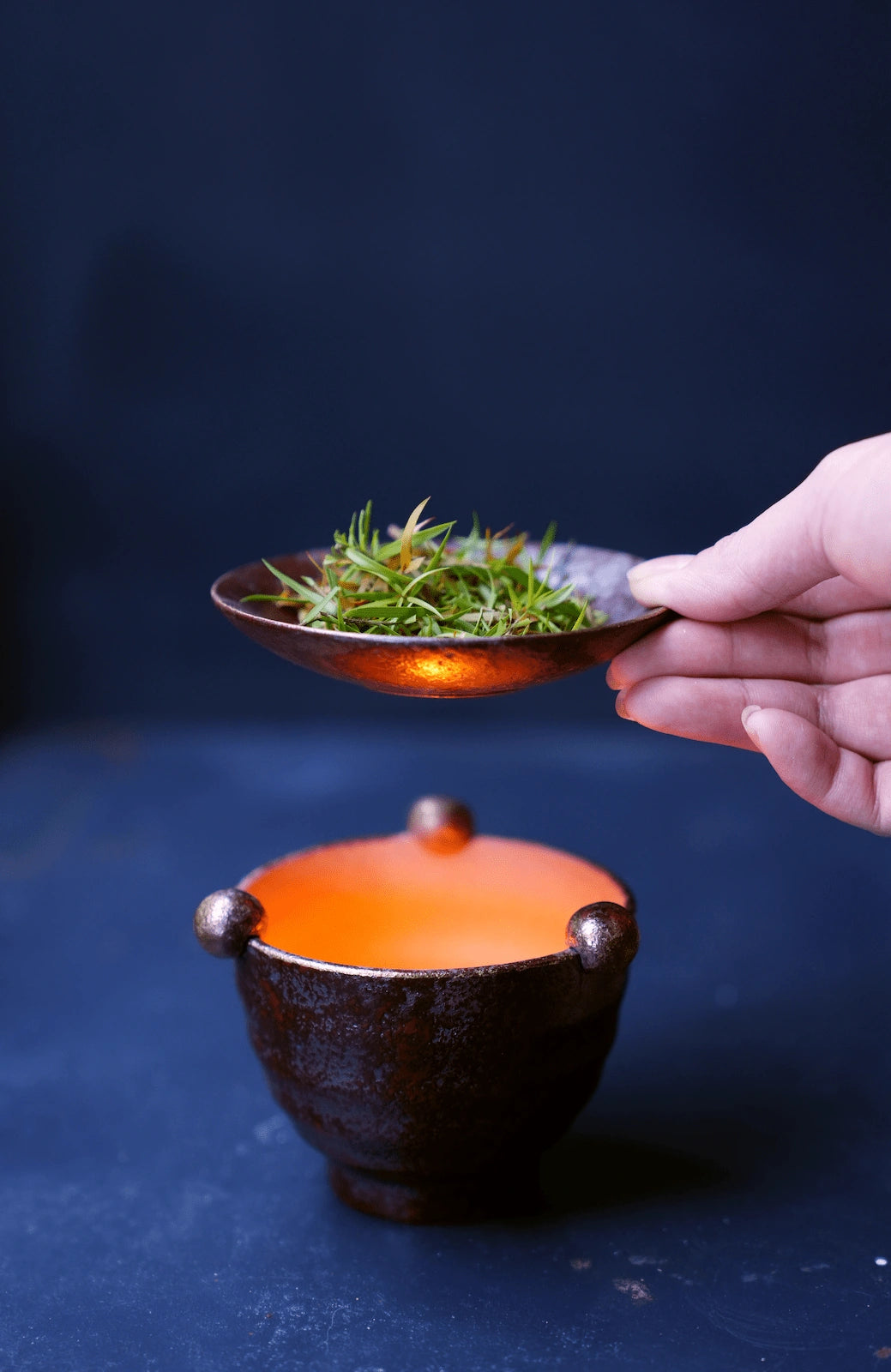Hand lifting ceramic dish from lit oil burner, dark background